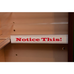 a sign holder shelf edge that holds a sign that reads "notice this!"